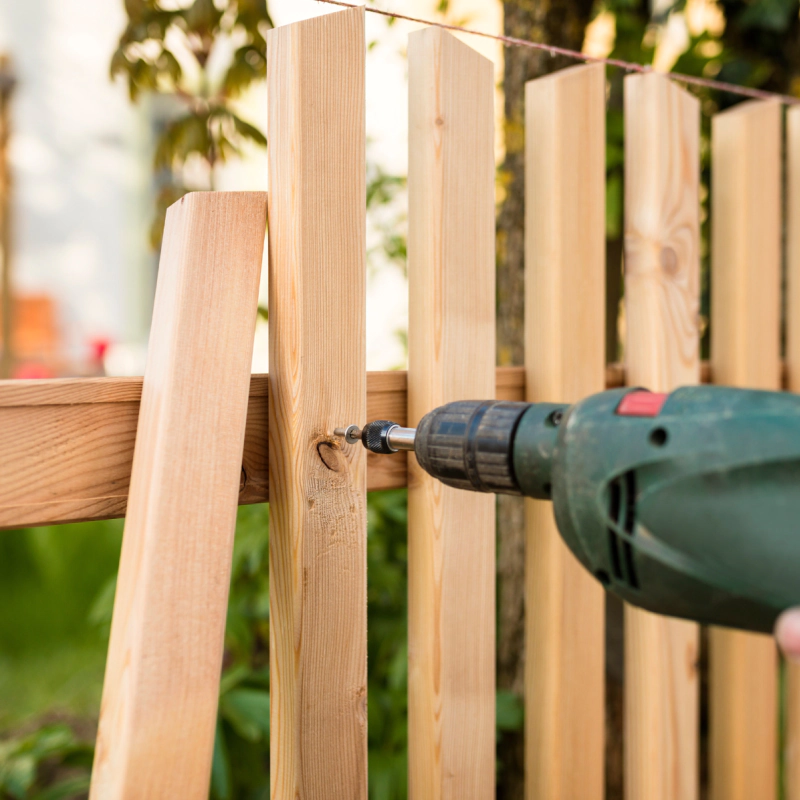 man drilling wood fence